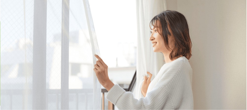 窓辺でカーテンを開く女性